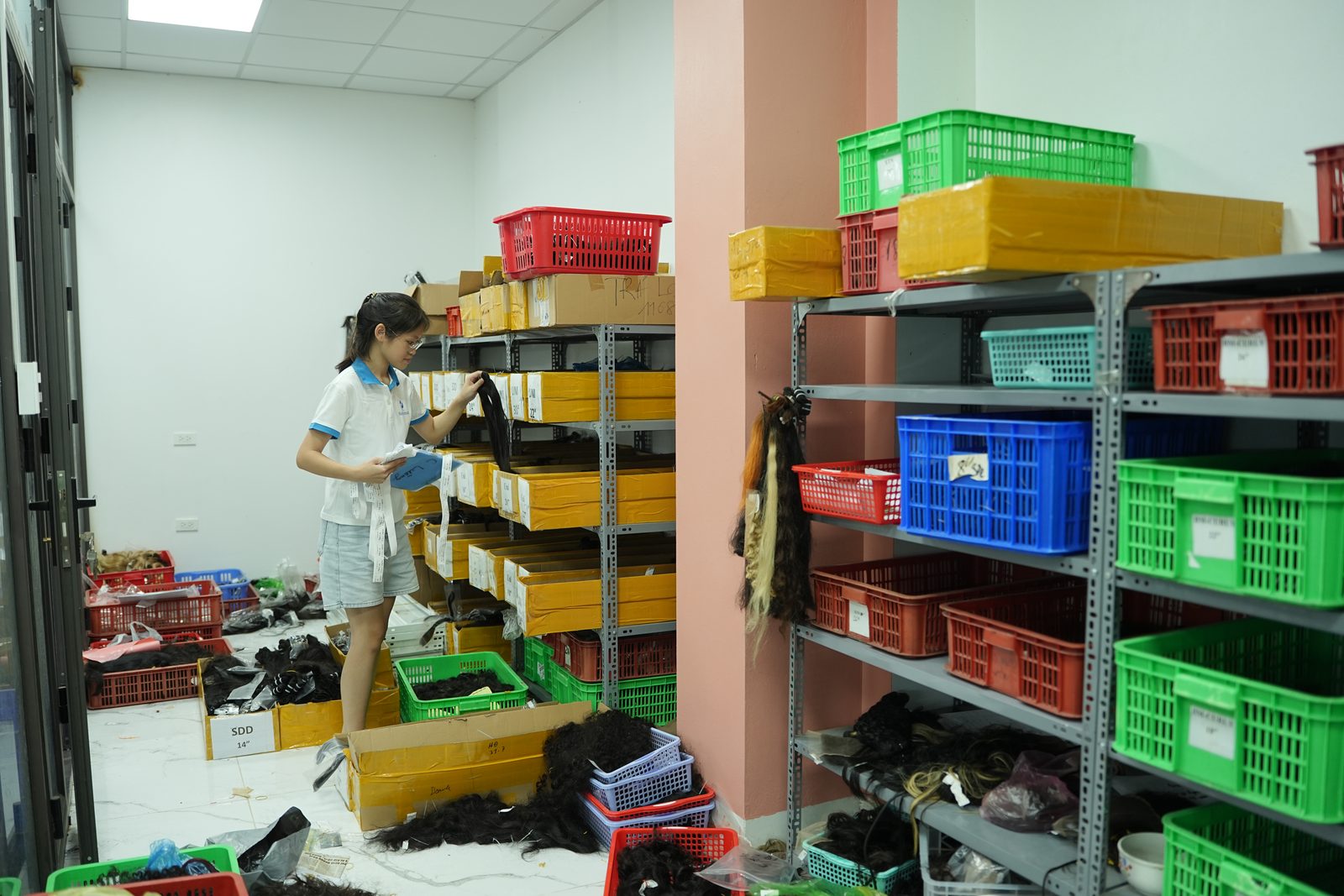 A staff member picks cartons from storeroom shelves stacked with labeled boxes and colored crates