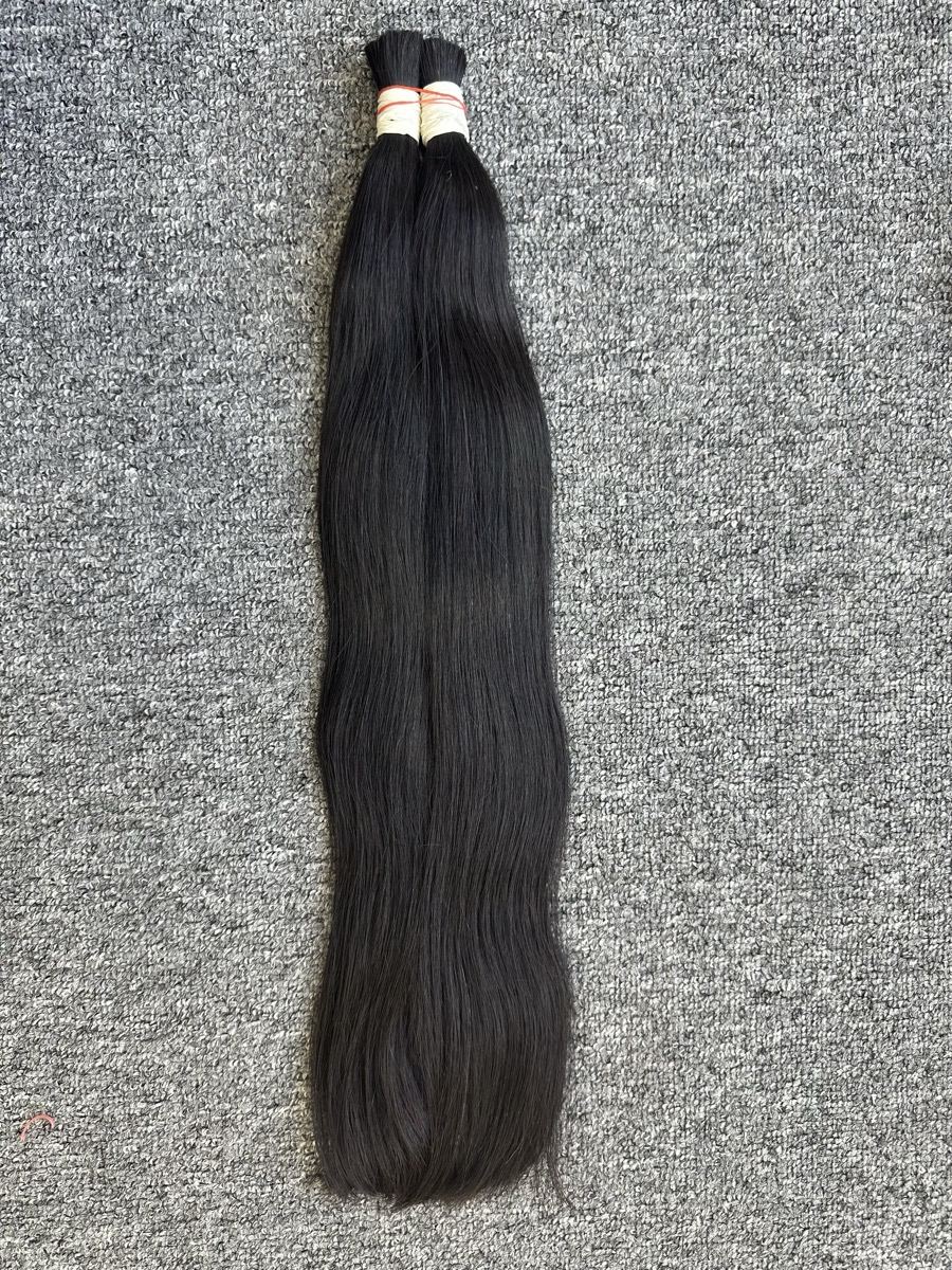 Two tied bunches of long straight dark bulk hair laid on a gray carpet
