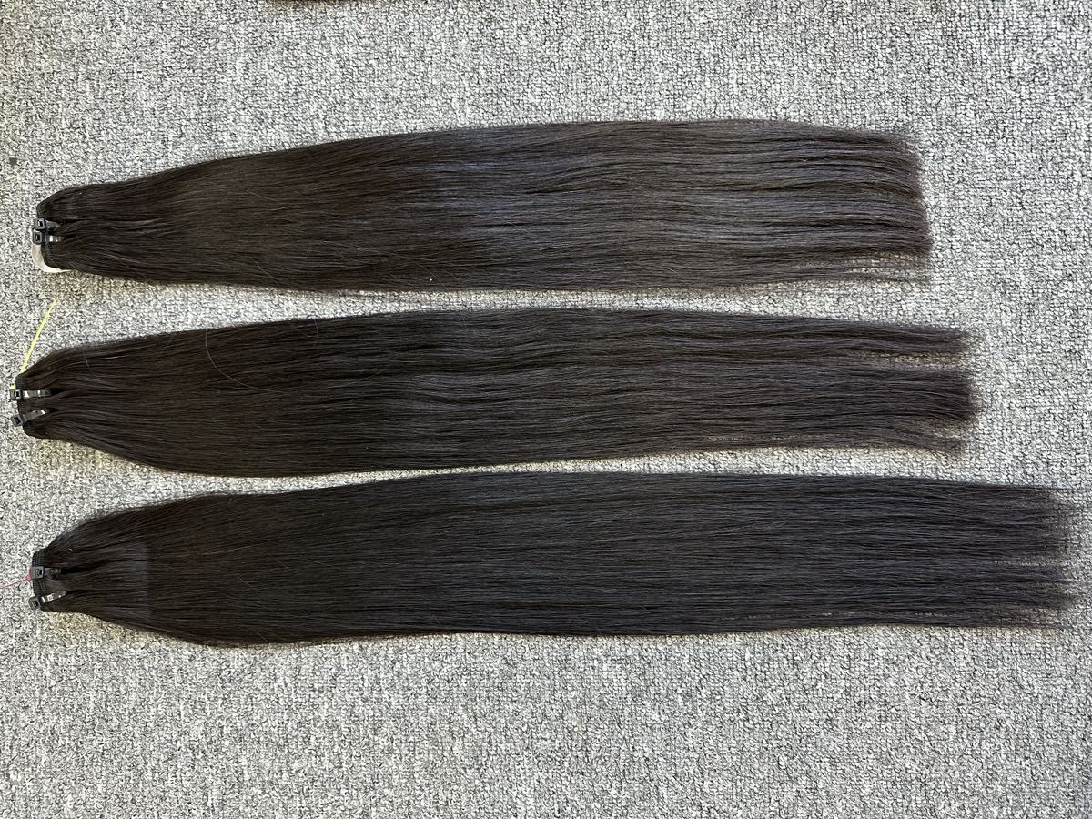 Three straight dark hair wefts of different lengths laid side by side on a gray carpet