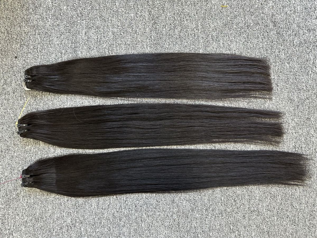Three long straight dark hair wefts laid side by side on a gray carpet